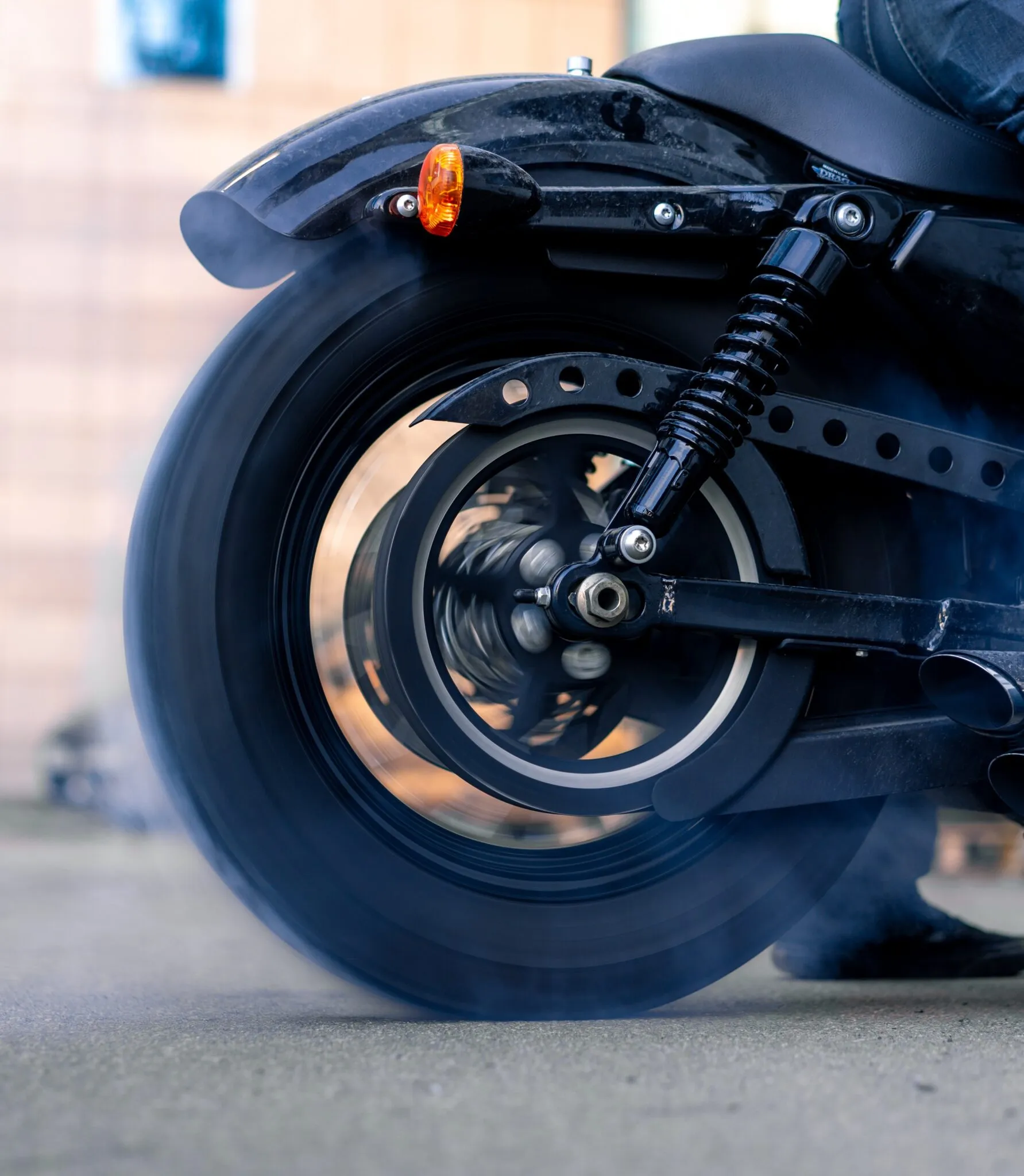 Rear wheel of a black Harley spinning in a burnout, tire smoke rising